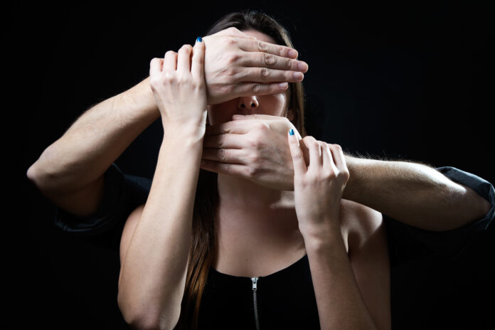 Young woman with eyes and mouth covered by a male hands. Handlin