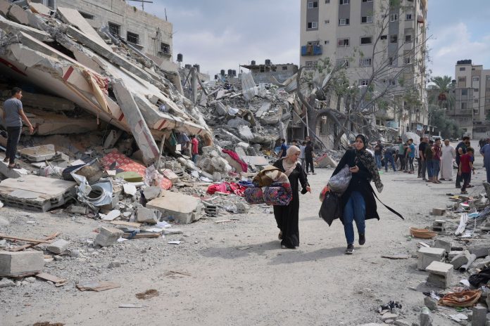 Palestinian women walk by buildings destroyed in Israeli airstrikes in Nuseirat camp in the central Gaza Strip, October 16, 2023. © 2023 Hatem Moussa_AP