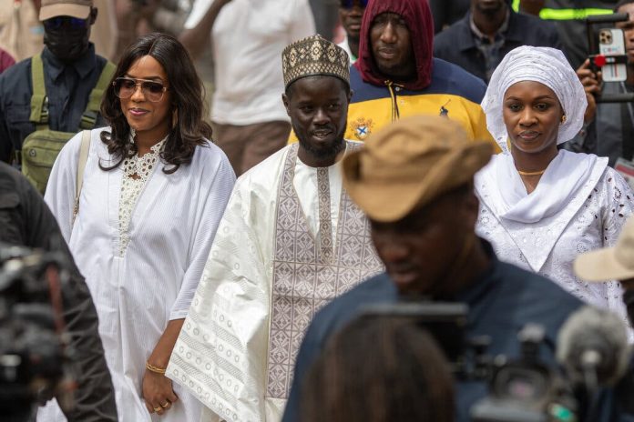 Photo_ The president-elect of Senegal stands with his two wives, all dressed in white...Credit...Jerome