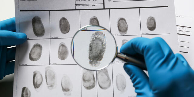 Criminalist exploring fingerprints with magnifying glass, closeu