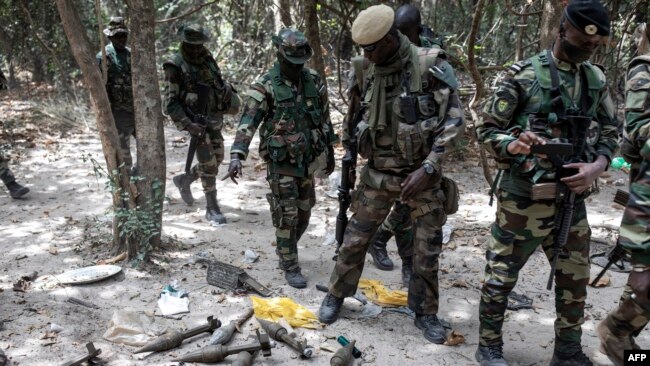 FILE - Members of the Senegalese Armed Forces walk past discarded rockets at a recently captured Movement of Democratic Forces of Casamance (MFDC) rebel base in Blaze Forest, Feb. 9, 2021